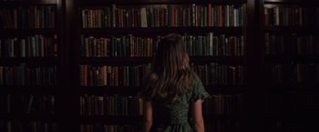 Movie still from “Shelter in Place” (2021), directed by Connor Martin – A woman standing in front of a book shelf filled with lots of books; Medium shot, High angle