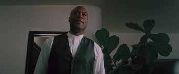 Movie still from “Shelter in Place” (2021), directed by Connor Martin – A man standing in front of a green plant; Medium shot, Low angle