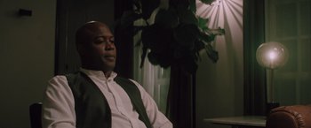 Movie still from “Shelter in Place” (2021), directed by Connor Martin – A man sitting in front of a plant in a living room; Medium shot, Over the shoulder angle