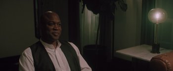 Movie still from “Shelter in Place” (2021), directed by Connor Martin – A man sitting in front of a plant in a dark room; Close Up shot, Over the shoulder angle