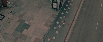 Movie still from “Shelter in Place” (2021), directed by Connor Martin – A person walking on a sidewalk with a bunch of stars on it; Extreme Wide shot, High angle
