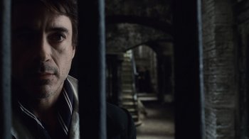 Movie still from “Sherlock Holmes” (2009), directed by Guy Ritchie – A man standing in a dark room with stairs in the background; Close Up shot, Over the shoulder angle