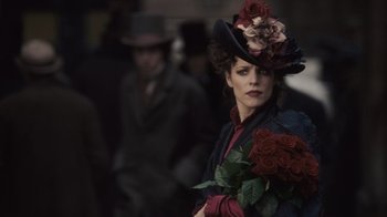 Movie still from “Sherlock Holmes” (2009), directed by Guy Ritchie – A woman in a hat holding a bunch of roses; Close Up shot, Over the shoulder angle