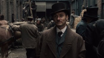 Movie still from “Sherlock Holmes” (2009), directed by Guy Ritchie – A man wearing a top hat standing in front of a group of people; Medium shot, Over the shoulder angle
