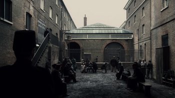 Movie still from “Sherlock Holmes” (2009), directed by Guy Ritchie – A group of people sitting in a courtyard; Extreme Wide shot, High angle