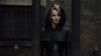 A woman in a black coat standing next to a brick wall