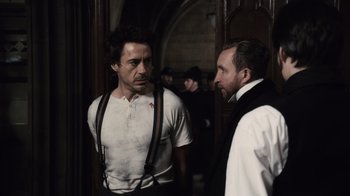 Movie still from “Sherlock Holmes” (2009), directed by Guy Ritchie – Two men standing next to each other in front of a wall; Medium shot, Over the shoulder angle