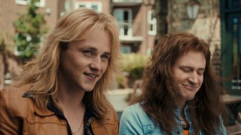 Movie still from “Bohemian Rhapsody” (2018), directed by Bryan Singer – Two young women standing next to each other on the sidewalk; Close Up shot, Over the shoulder angle