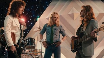 Movie still from “Bohemian Rhapsody” (2018), directed by Bryan Singer – A group of people that are standing up in a room; Medium shot, Over the shoulder angle