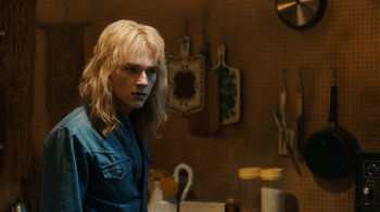 Movie still from “Bohemian Rhapsody” (2018), directed by Bryan Singer – A man with long blonde hair standing in a kitchen; Medium shot, Over the shoulder angle