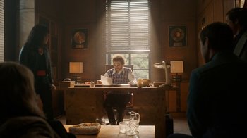 Movie still from “Bohemian Rhapsody” (2018), directed by Bryan Singer – A man sitting at a desk in front of a laptop computer; Wide shot, Low angle