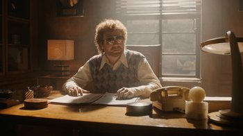 Movie still from “Bohemian Rhapsody” (2018), directed by Bryan Singer – An older man sitting at a desk in front of a phone; Medium shot, Low angle