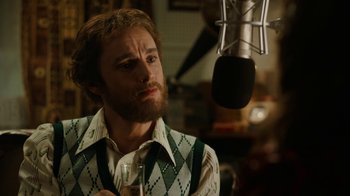 Movie still from “Bohemian Rhapsody” (2018), directed by Bryan Singer – A man with a beard is standing in front of a microphone; Close Up shot, Over the shoulder angle