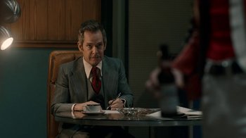 Movie still from “Bohemian Rhapsody” (2018), directed by Bryan Singer – A man sitting at a table writing on a piece of paper; Medium shot, Over the shoulder angle