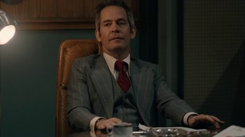 Movie still from “Bohemian Rhapsody” (2018), directed by Bryan Singer – A man sitting at a table in a suit and tie; Medium shot, Low angle