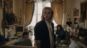 Movie still from “Bohemian Rhapsody” (2018), directed by Bryan Singer – A man standing in front of other people in a living room; Medium shot, Over the shoulder angle