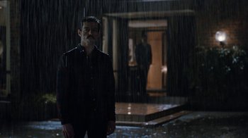 Movie still from “Bohemian Rhapsody” (2018), directed by Bryan Singer – A man standing in the rain in front of a building; Wide shot, Over the shoulder angle