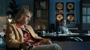 Movie still from “Bohemian Rhapsody” (2018), directed by Bryan Singer – A woman sitting in front of a man sitting in front of a desk; Medium shot, Over the shoulder angle