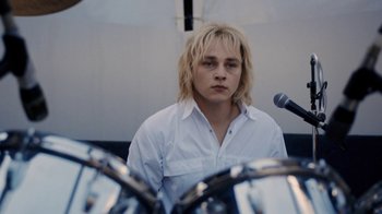 Movie still from “Bohemian Rhapsody” (2018), directed by Bryan Singer – A man with blonde hair is standing in front of a microphone; Close Up shot, Over the shoulder angle