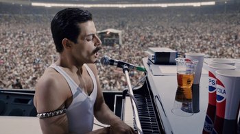 Movie still from “Bohemian Rhapsody” (2018), directed by Bryan Singer – A man with a microphone is singing at a concert; Medium shot, Over the shoulder angle