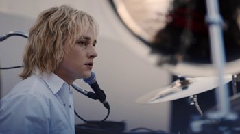 Movie still from “Bohemian Rhapsody” (2018), directed by Bryan Singer – A man with blonde hair is holding a microphone; Close Up shot, Over the shoulder angle