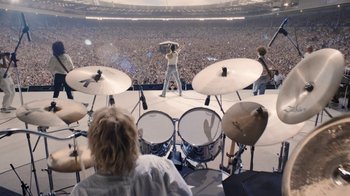 Movie still from “Bohemian Rhapsody” (2018), directed by Bryan Singer – A man is playing drums in front of an audience; Extreme Wide shot, High angle