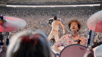 Movie still from “Bohemian Rhapsody” (2018), directed by Bryan Singer – A man in a crowd of people playing drums and singing; Medium shot, Over the shoulder angle