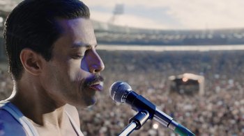 Movie still from “Bohemian Rhapsody” (2018), directed by Bryan Singer – A person holding a microphone on a stage; Close Up shot, Over the shoulder angle