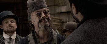 Movie still from “Sherlock Holmes: A Game of Shadows” (2011), directed by Guy Ritchie – A man with long hair and a goatee is smiling; Close Up shot, Over the shoulder angle