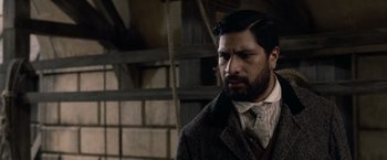 Movie still from “Sherlock Holmes: A Game of Shadows” (2011), directed by Guy Ritchie – A man in a suit and tie standing next to a brick wall; Close Up shot, Over the shoulder angle