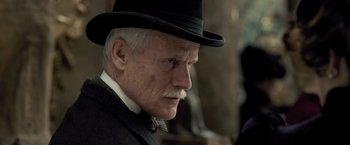 Movie still from “Sherlock Holmes: A Game of Shadows” (2011), directed by Guy Ritchie – An older man wearing a black hat and a black suit; Close Up shot, Low angle