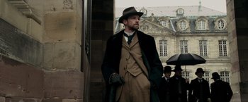 Movie still from “Sherlock Holmes: A Game of Shadows” (2011), directed by Guy Ritchie – A man with a beard and a hat is standing in the street; Medium shot, Low angle