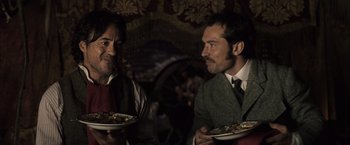 Movie still from “Sherlock Holmes: A Game of Shadows” (2011), directed by Guy Ritchie – Two men are holding plates of food in front of each other; Medium shot, Over the shoulder angle