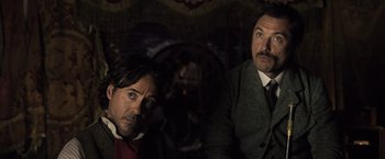Movie still from “Sherlock Holmes: A Game of Shadows” (2011), directed by Guy Ritchie – Two men are standing next to each other in a dark room; Medium shot, Low angle