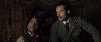 Movie still from “Sherlock Holmes: A Game of Shadows” (2011), directed by Guy Ritchie – Two men are sitting next to each other in a room; Medium shot, Low angle