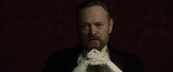 Movie still from “Sherlock Holmes: A Game of Shadows” (2011), directed by Guy Ritchie – A man with a beard wearing white gloves and a black suit; Close Up shot, Low angle