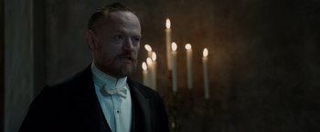 Movie still from “Sherlock Holmes: A Game of Shadows” (2011), directed by Guy Ritchie – A man with a beard wearing a suit and bow tie in front of candles in a room; Medium shot, Low angle