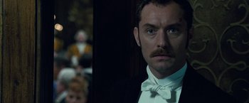 Movie still from “Sherlock Holmes: A Game of Shadows” (2011), directed by Guy Ritchie – A person wearing a suit and a bow tie; Close Up shot, Over the shoulder angle