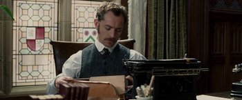 Movie still from “Sherlock Holmes: A Game of Shadows” (2011), directed by Guy Ritchie – A man sitting at a table looking down at a piece of paper; Medium shot, High angle