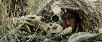 Movie still from “Shooter” (2007), directed by Antoine Fuqua – A man in a ghillie suit with a rifle; Close Up shot, Over the shoulder angle