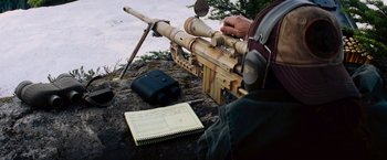 Movie still from “Shooter” (2007), directed by Antoine Fuqua – A man that is sitting on a rock with a rifle; Medium shot, High angle