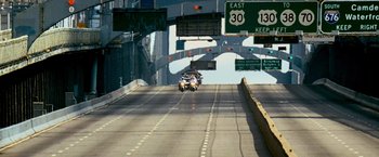 Movie still from “Shooter” (2007), directed by Antoine Fuqua – A car driving down a street under a bridge; Extreme Wide shot, High angle
