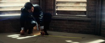 A man in a black suit is measuring a brick wall