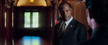 Movie still from “Shooter” (2007), directed by Antoine Fuqua – A man in a suit and tie standing in front of an american flag; Close Up shot, Low angle