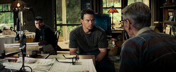 Movie still from “Shooter” (2007), directed by Antoine Fuqua – A man sitting in front of a table with glasses on top of it; Medium shot, Over the shoulder angle