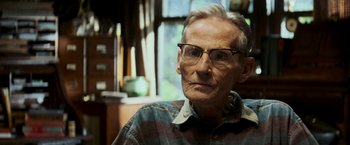 Movie still from “Shooter” (2007), directed by Antoine Fuqua – An older man wearing glasses sitting in front of a window; Close Up shot, Over the shoulder angle