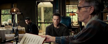 Movie still from “Shooter” (2007), directed by Antoine Fuqua – A man sitting at a table with a sheet of paper; Medium shot, Over the shoulder angle