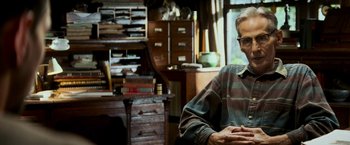 Movie still from “Shooter” (2007), directed by Antoine Fuqua – A man sitting in front of a desk in a room; Close Up shot, Low angle