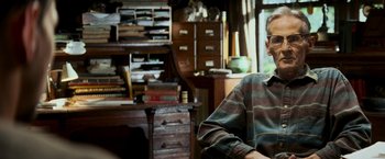 Movie still from “Shooter” (2007), directed by Antoine Fuqua – An older man sitting in a chair in front of a desk; Close Up shot, Over the shoulder angle