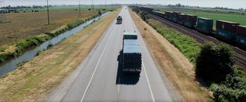 Movie still from “Shooter” (2007), directed by Antoine Fuqua – A truck driving down a road with a train on it's side; Extreme Wide shot, High angle